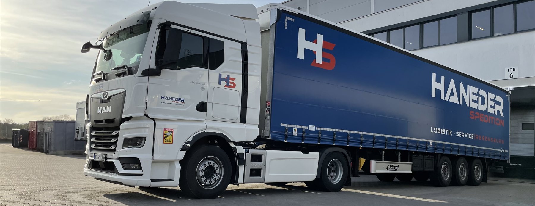 HANEDER MAN TGX mit blauem Planenauflieger am Tor des Logistikzentrums